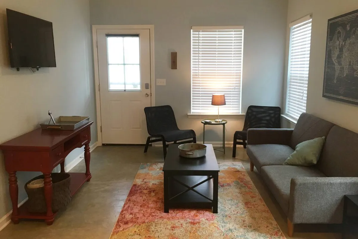 A cozy living space centered around a comfortable sofa and coffee table, accented by a warm lampshade and a soft rug. The area is designed for relaxation, conversation, or casual gatherings, offering an inviting ambiance for family or friends to unwind together.
