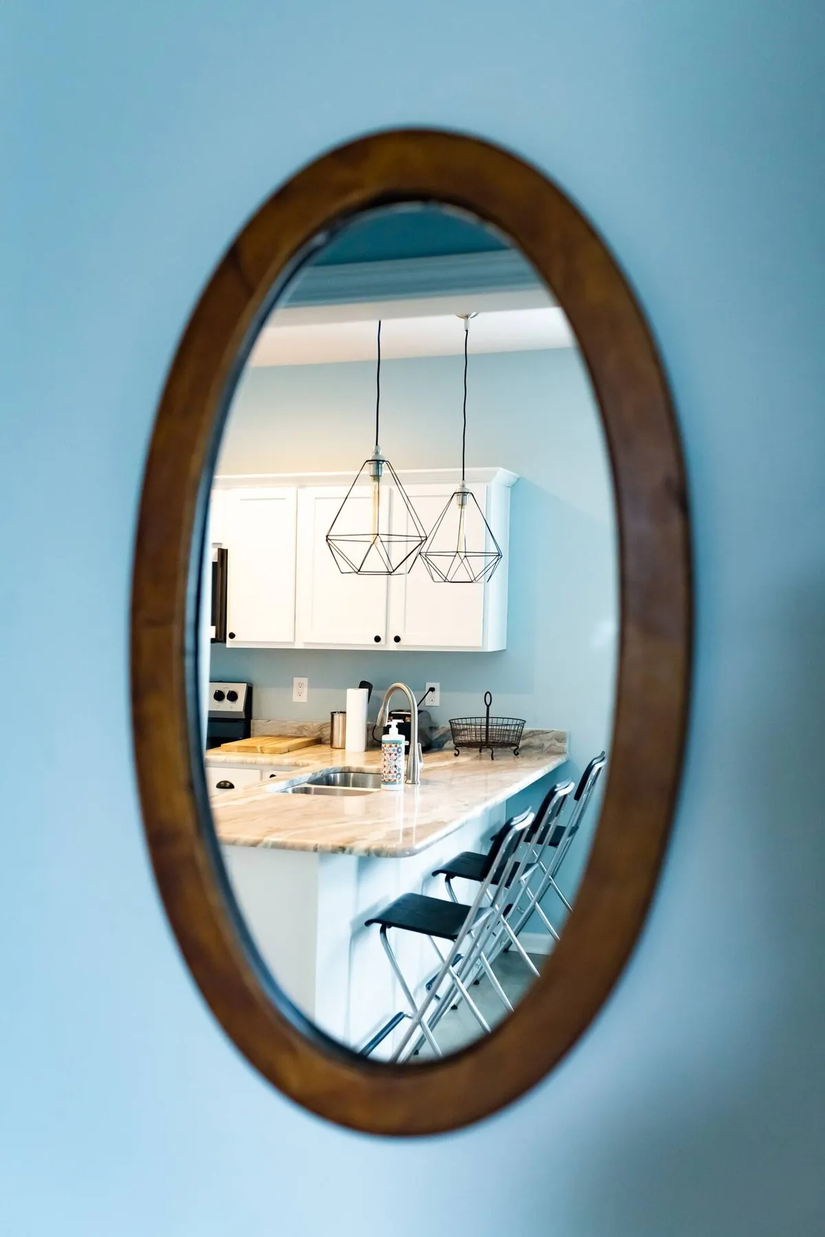 An inviting scene of the kitchen island framed by pendant lights, with an oval mirror reflecting additional kitchen features. The setup hints at a space ideal for cooking, entertaining, and socializing, with ample counter space and modern design elements.