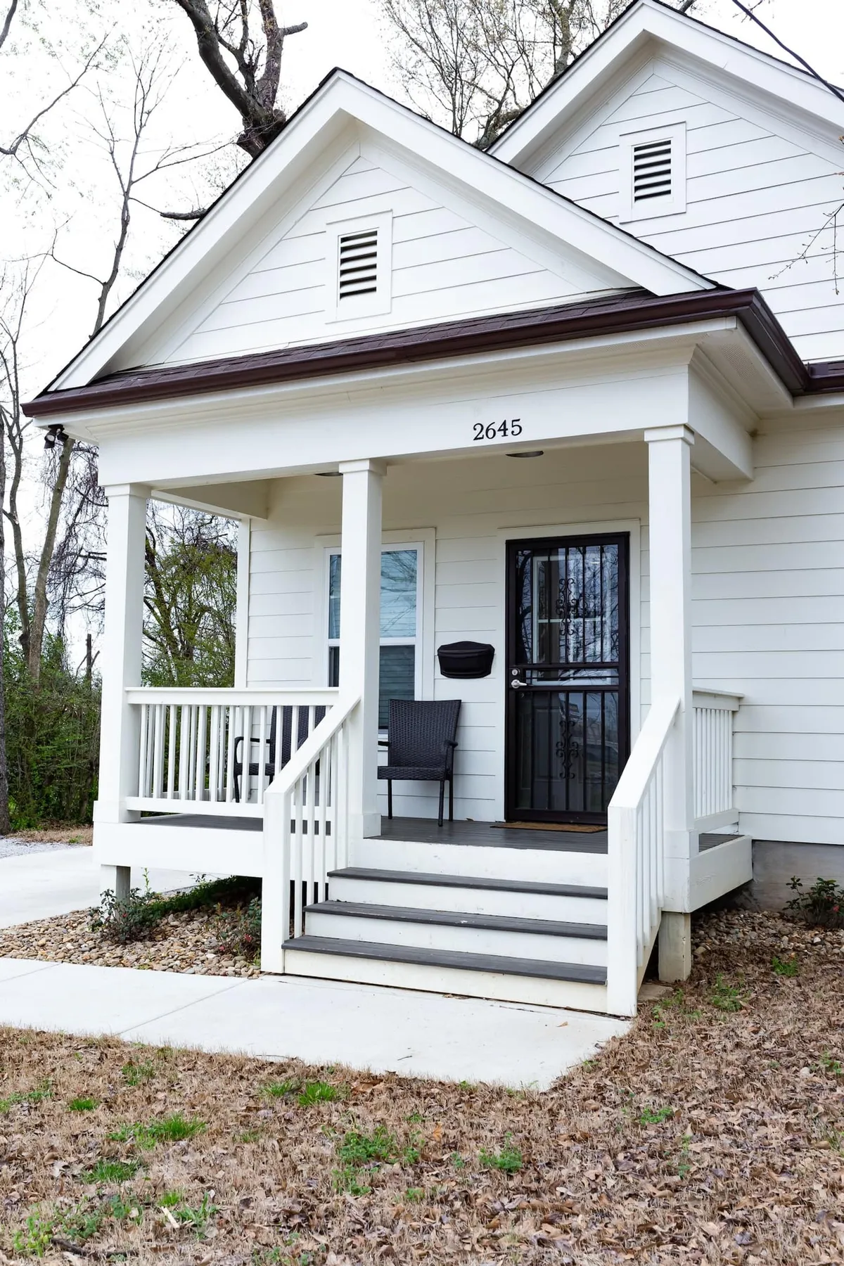 This image features the front porch of the property, with a prominent black door and the house number 2645 visible. A classic rocking chair sits on the porch, inviting guests to unwind outdoors. The overall scene appears calm and welcoming, offering a glimpse of the home's curb appeal and a potential spot for relaxation or informal meetings.
