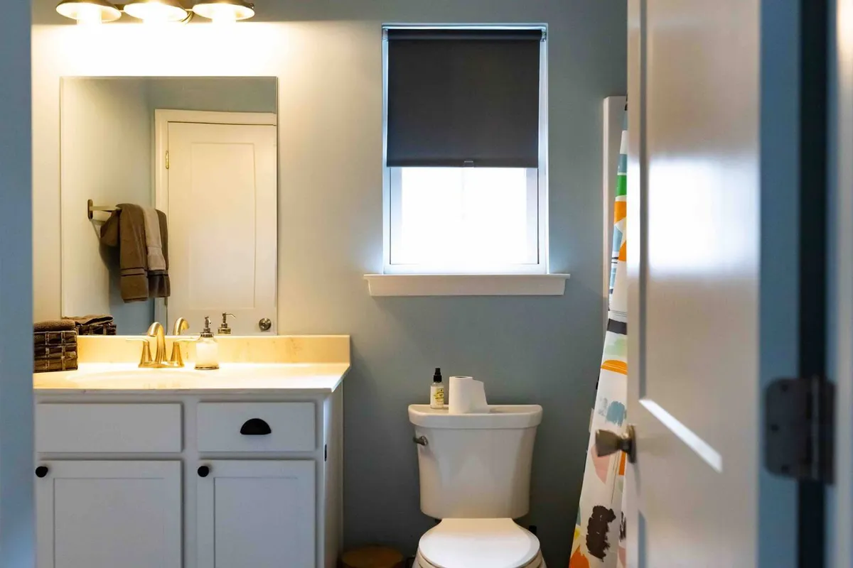 A modern bathroom bathed in soft natural light, featuring a stylish sink, toilet, mirror, and a window. The fresh ambiance and thoughtful design invite guests to unwind and prepare for the day or evening.