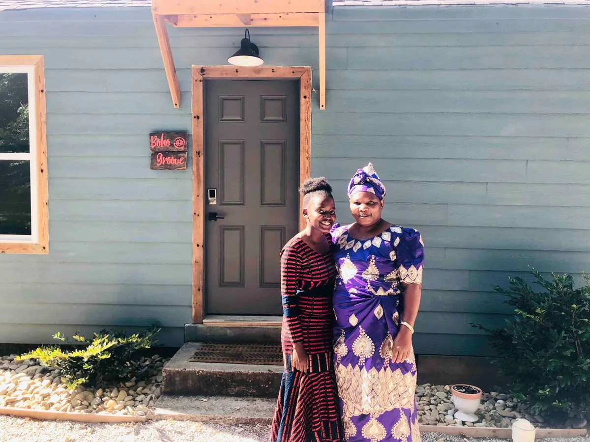 This exterior image features the front door of the house, with two women in traditional attire standing by a decorative sign. The scene is lively and joyful, evoking a sense of community and celebration. The image hints at the home's proximity to local arts and cultural experiences, as well as its inviting atmosphere for gathering and exploration.