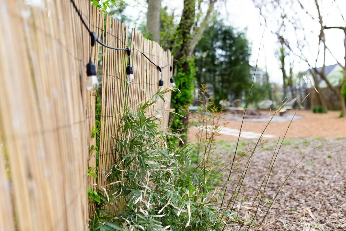 A tranquil outdoor space bordered by a bamboo fence and strung with hanging lights, surrounded by lush greenery. The scene suggests an inviting, nature-inspired retreat for outdoor gatherings or quiet relaxation after a day exploring the city.