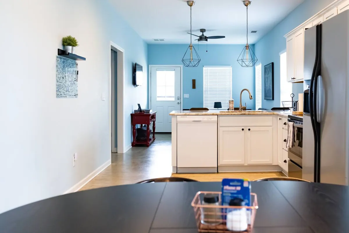 A welcoming view of the open kitchen and dining area, with a kitchen island, dining table, decorative wall art, and sightlines to the entrance. The setup is ideal for meal prep, shared dining, and socializing, fostering a sense of flow and connection throughout the communal areas.