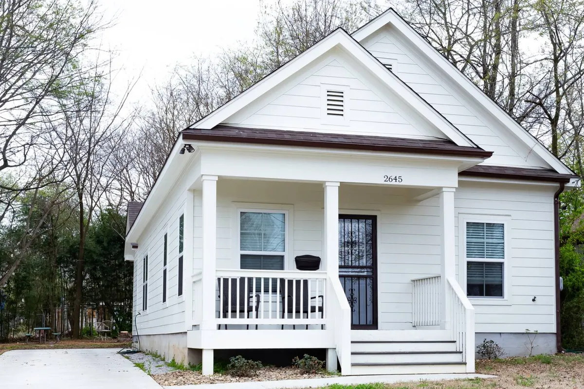 A welcoming view of the home’s white exterior and front porch, complete with a black front door. The porch provides space for relaxing, socializing, and enjoying the friendly neighborhood atmosphere after a night out.