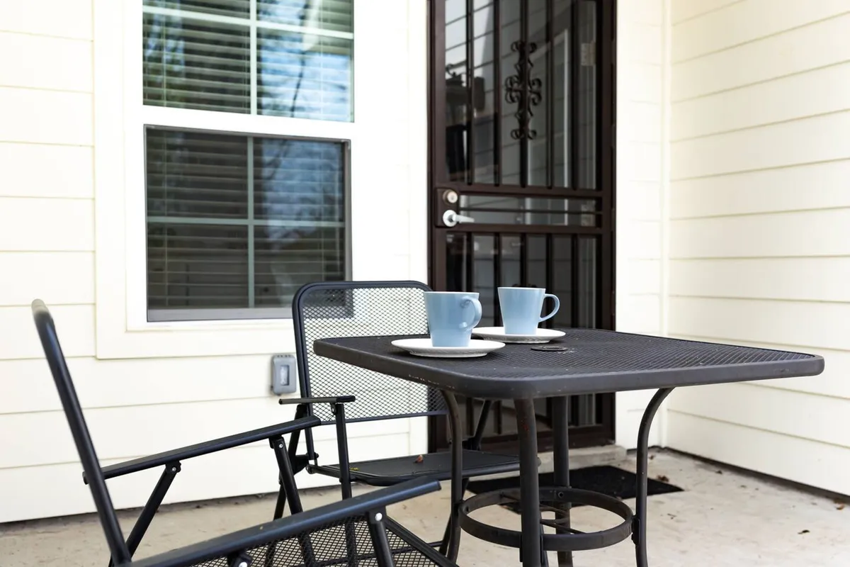 A close-up view of a table with coffee cups and chairs set on the front porch, with the front door visible in the background. The scene radiates a relaxed atmosphere, perfect for morning coffee, informal conversations, or unwinding after a day of work.